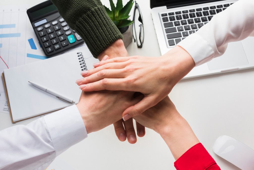 Business team stacking hands together symbolizing teamwork, employee benefits plan collaboration, and payroll savings solutions